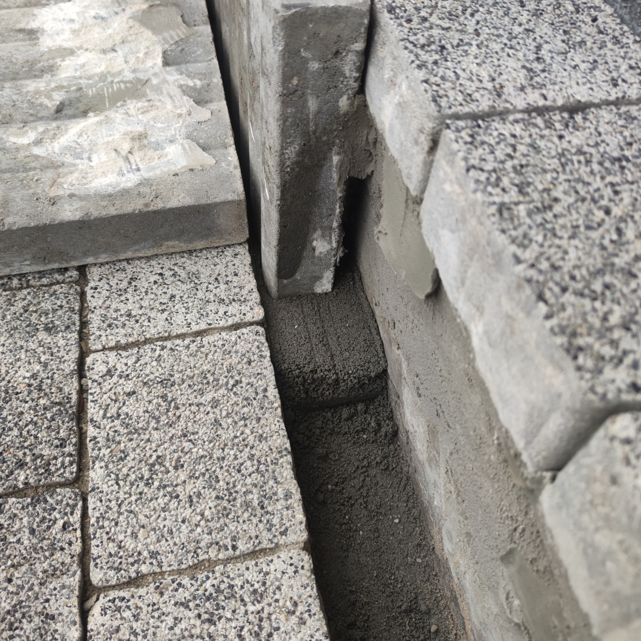 Układanie szarej kostki brukowej, widoczne wypełnienie spoin piaskiem, fragment z białymi zabrudzeniami na jednej z kostek.
