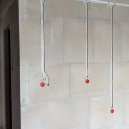 Power-gdansk - Białe kable elektryczne prowadzone po ścianie z bloków betonowych, z widocznymi puszkami instalacyjnymi zabezpieczonymi czerwonymi zaślepkami.