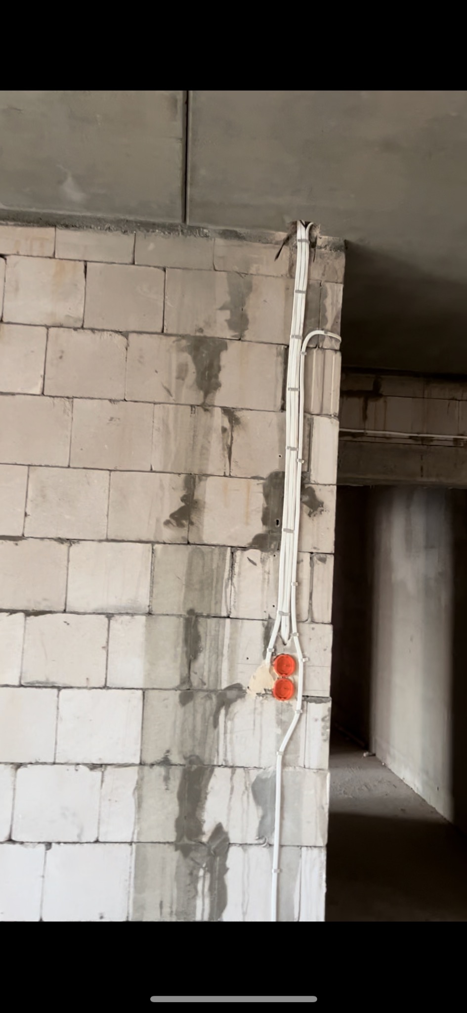 Białe kable elektryczne prowadzone po ścianie z betonu komórkowego, z zamontowanymi pomarańczowymi puszkami instalacyjnymi, widoczne ślady po zaprawie murarskiej.