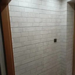 Ściana wykończona dekoracyjną cegłą w odcieniach bieli, widoczny włącznik światła i fragment ościeżnicy w Suchorze.