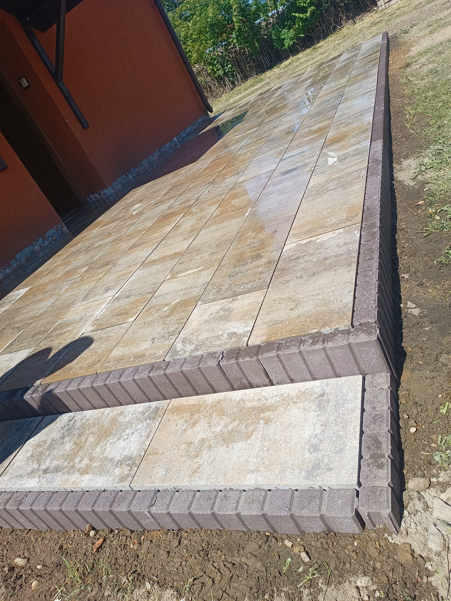 Ułożona kostka brukowa tworząca schody i chodnik przy budynku, z widocznymi brązowymi obrzeżami i wzorem imitującym kamień.