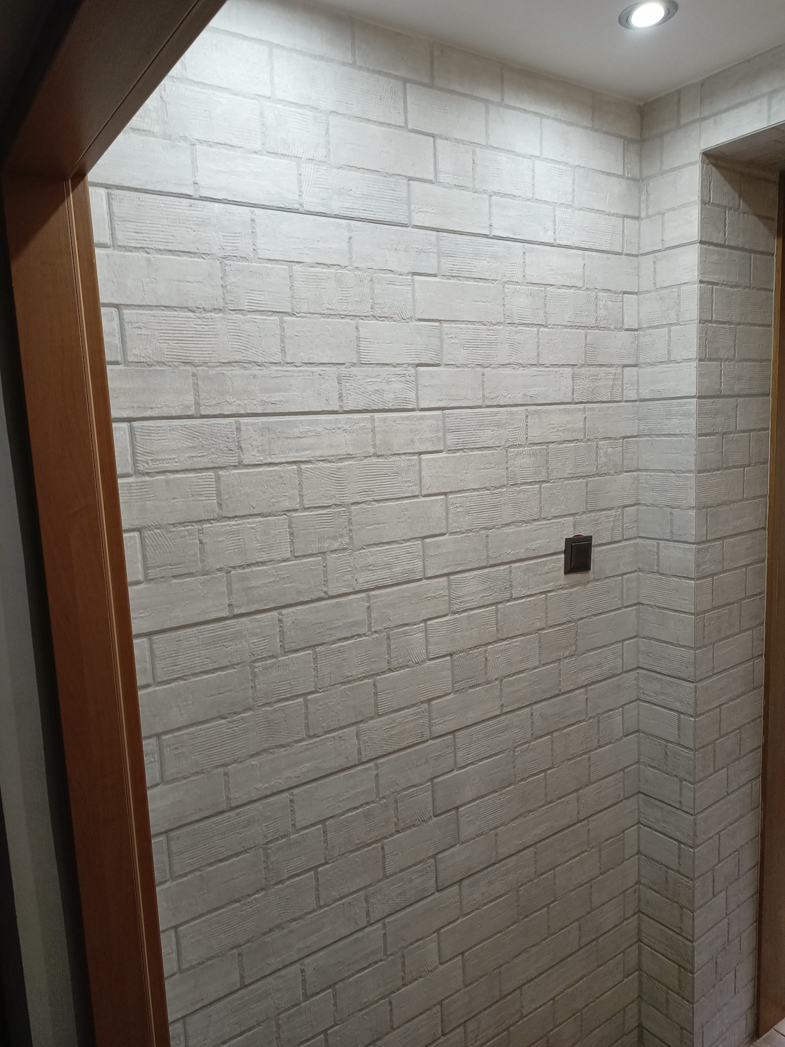 Ściana wykończona dekoracyjną cegłą w odcieniach bieli, widoczny włącznik światła i fragment ościeżnicy w Suchorze.