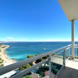 Widok z balkonu apartamentu na morze, z widoczną linią brzegową, plażą i żaglówką w oddali.