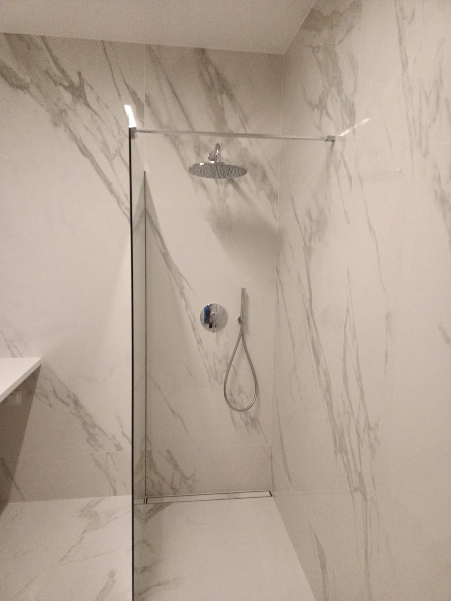 Nowoczesna kabina prysznicowa typu walk-in z deszczownicą, wykończona białymi płytkami imitującymi marmur, zrealizowana w łazience w Warszawie.