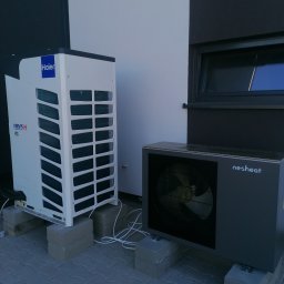 Eko-Mont- Klimatyzacja Wentylacja - Dwa moduły klimatyzacji zewnętrznej, Haier i nesheat, umieszczone na betonowych bloczkach przed budynkiem z szarą kostką brukową.