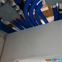 Eko-Mont- Klimatyzacja Wentylacja - Instalacja systemu rekuperacji z niebieskimi rurami karbowanymi i szarymi rozdzielaczami pod sufitem w trakcie montażu, widoczne elementy konstrukcji drewnianej stropu.