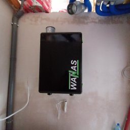 Eko-Mont- Klimatyzacja Wentylacja - Czarna skrzynka rekuperatora WANAS zamontowana na ścianie w pomieszczeniu w trakcie instalacji, widoczne rury wentylacyjne i izolacja stropu.