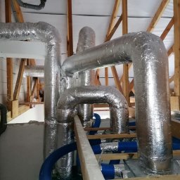 Eko-Mont- Klimatyzacja Wentylacja - Instalacja rekuperacji z rurami w izolacji aluminiowej i niebieskimi rurami wentylacyjnymi w domu w Kościanie, widok z dołu na drewnianą konstrukcję dachu.
