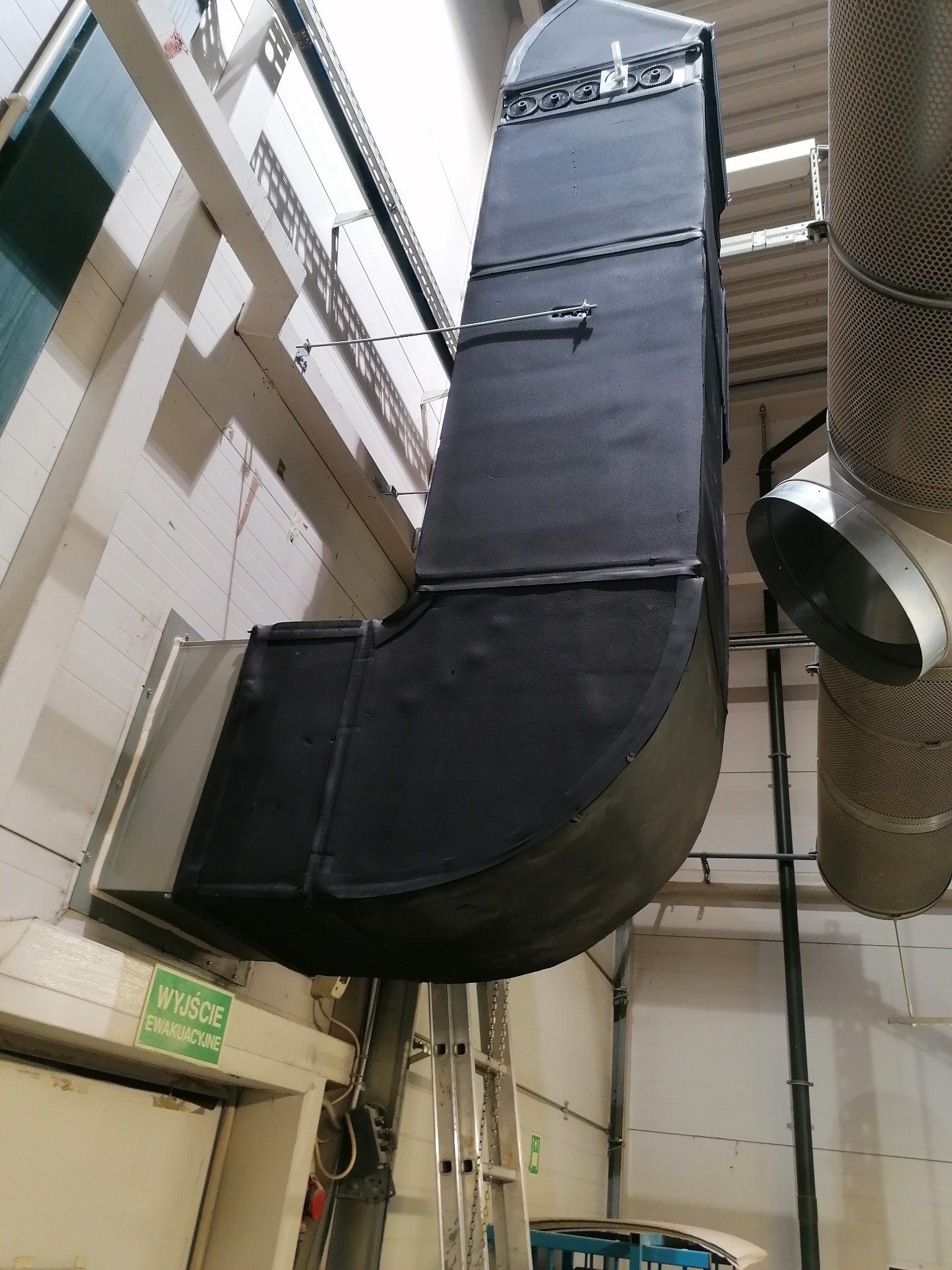 System kanałów wentylacyjnych w hali przemysłowej, widoczne elementy mocujące i filtry cylindryczne, z bliska.