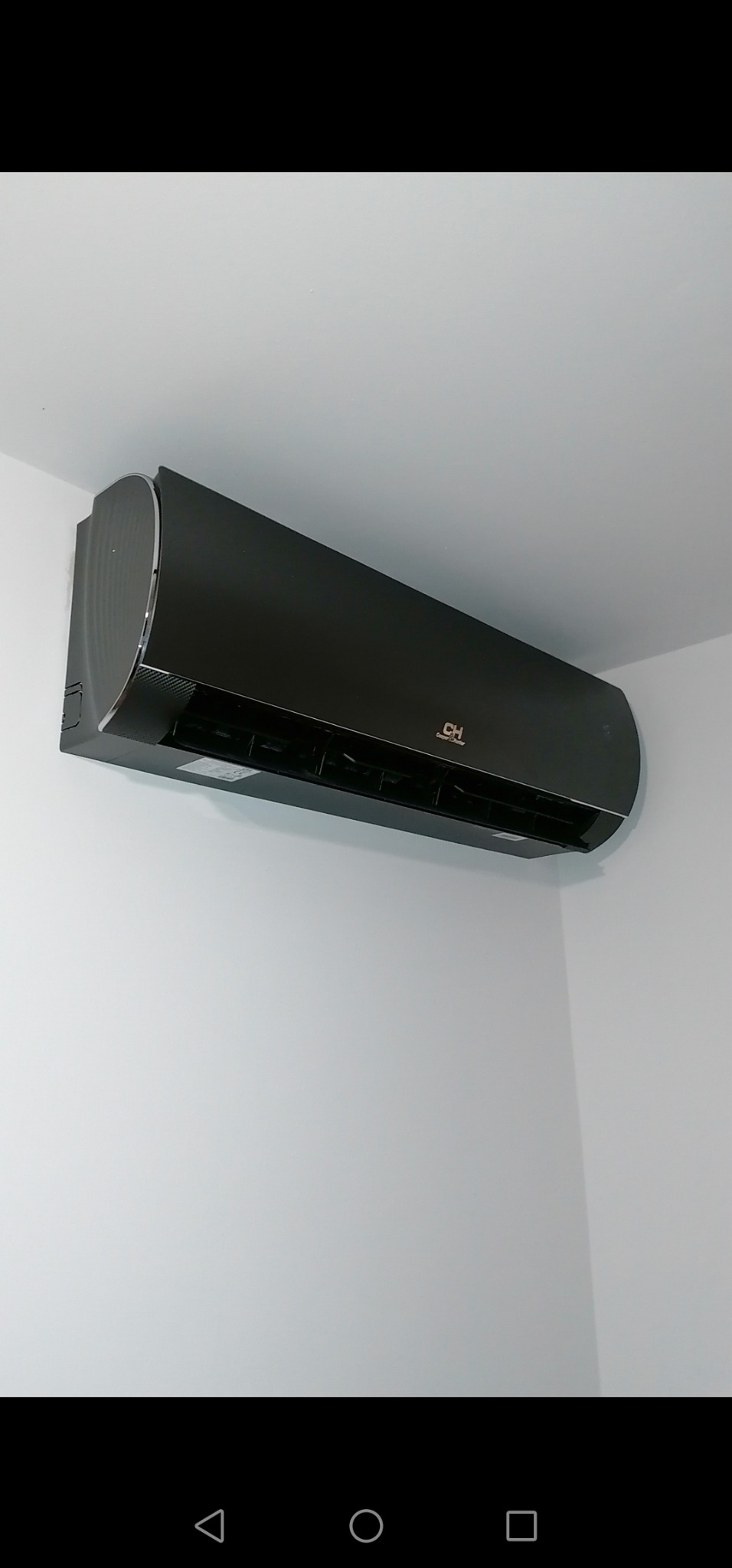 Czarna jednostka wewnętrzna klimatyzacji marki CH zamontowana na białej ścianie w rogu pomieszczenia.