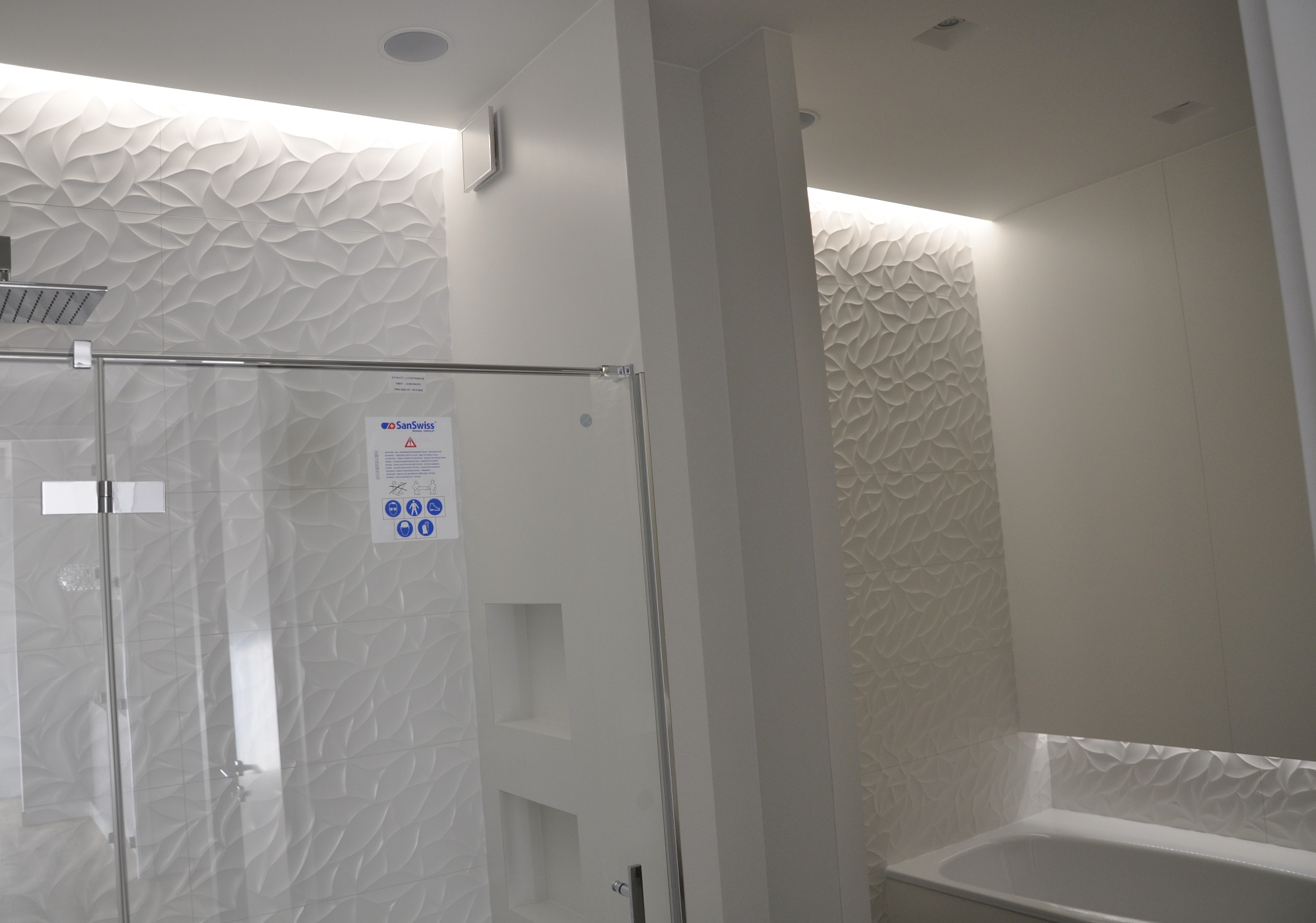 Biała łazienka z nowoczesnymi płytkami 3D w kształcie liści, przeszklona kabina prysznicowa, podświetlenie LED i wnęki w ścianie.