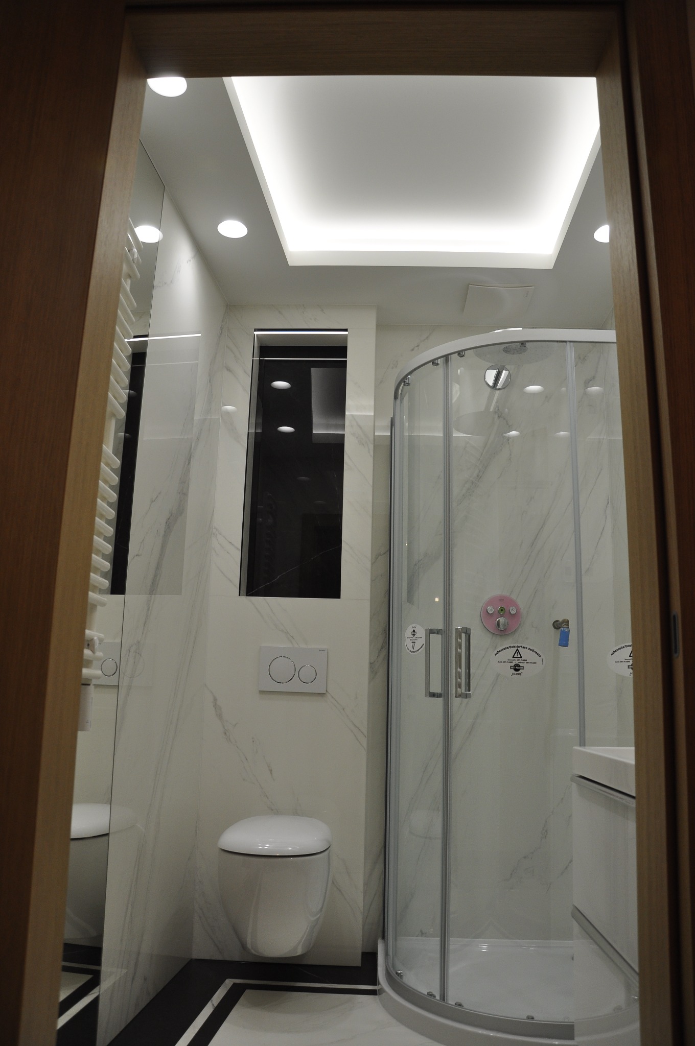 Nowoczesna łazienka z kabiną prysznicową z hydromasażem, podwieszaną toaletą i oświetleniem LED sufitowym, wykończona marmurową okładziną ścienną.