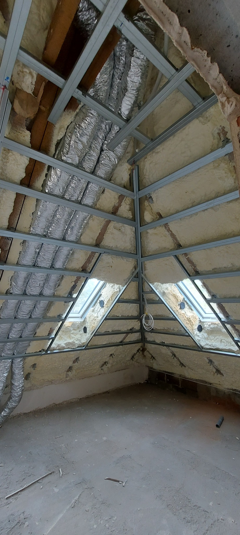 Adaptacja poddasza: izolacja natryskowa pianą PUR, widoczne okna dachowe, metalowa konstrukcja pod przyszłą zabudowę, rury wentylacyjne w folii aluminiowej.