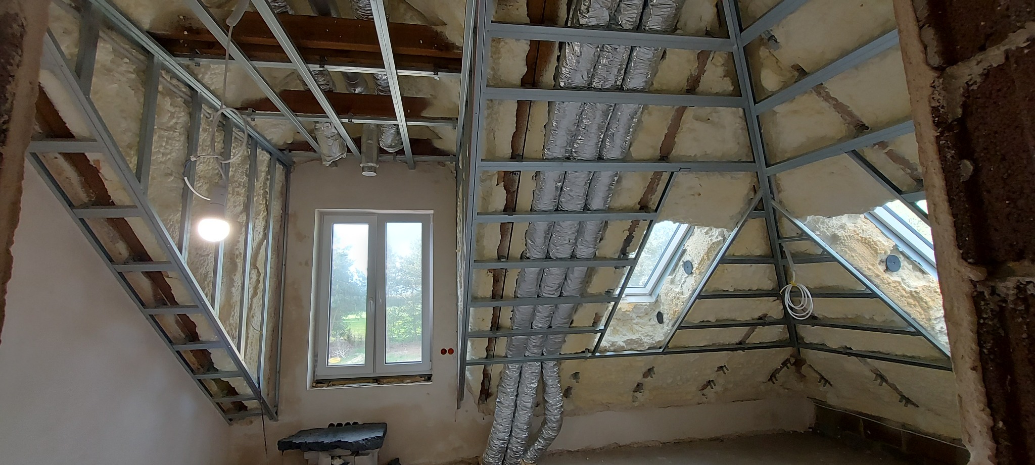 Montaż metalowej konstrukcji na poddaszu z widoczną izolacją termiczną, przewodami wentylacyjnymi i oknem dachowym.