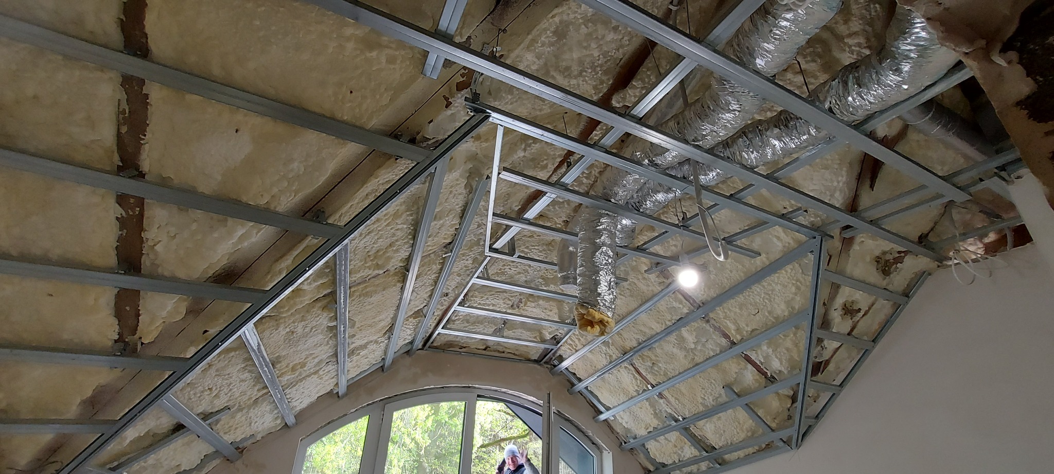 Montaż metalowej konstrukcji pod izolację poddasza z widocznymi przewodami wentylacyjnymi i oknem dachowym w tle.