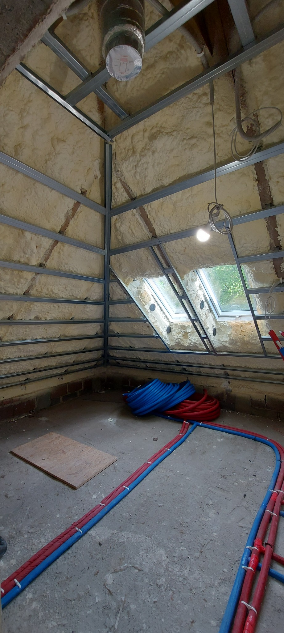 Poddasze w trakcie adaptacji: metalowa konstrukcja pod zabudowę, ocieplenie pianą natryskową, widoczne okna dachowe i instalacje wodne.