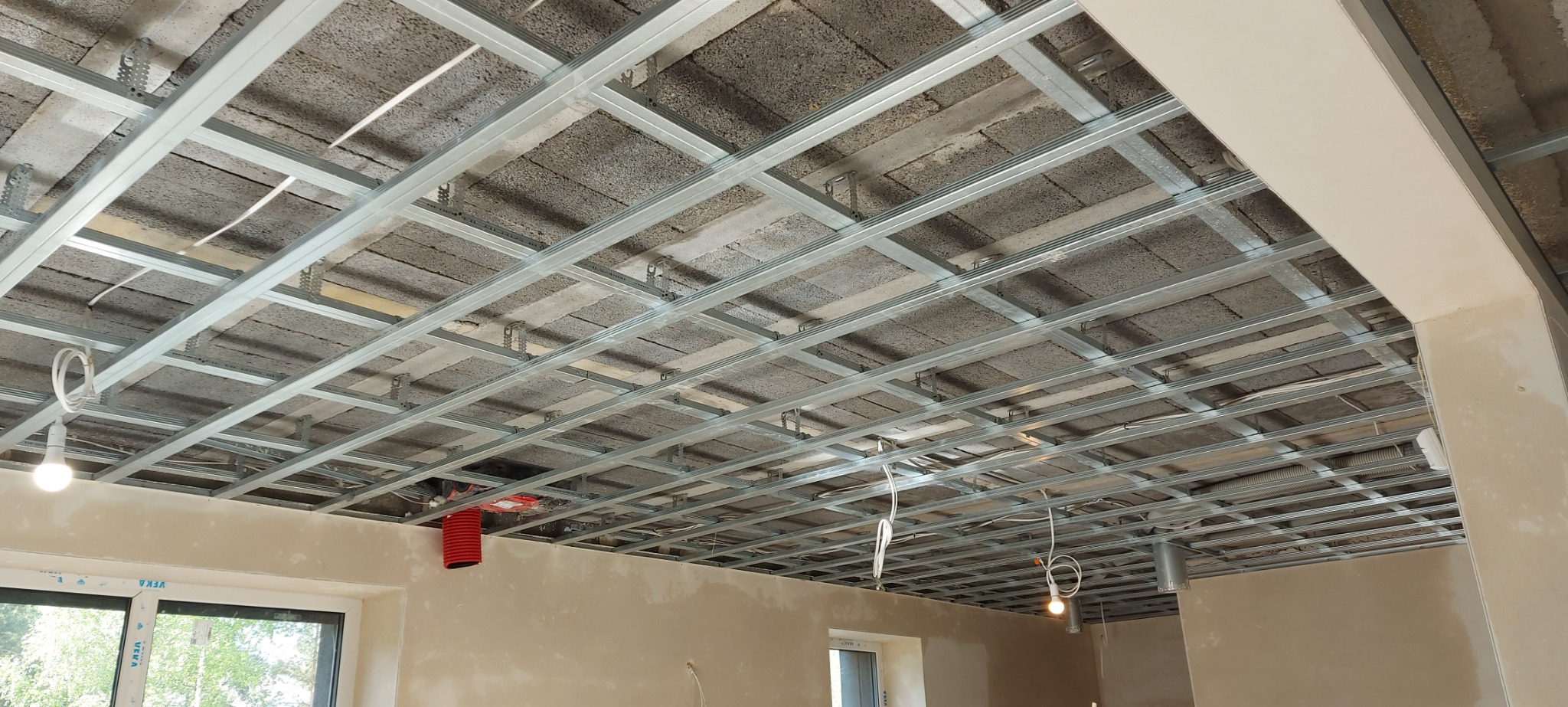 Metalowa konstrukcja podwieszanego sufitu zamontowana do betonowego stropu, widoczne przewody elektryczne i rury wentylacyjne.