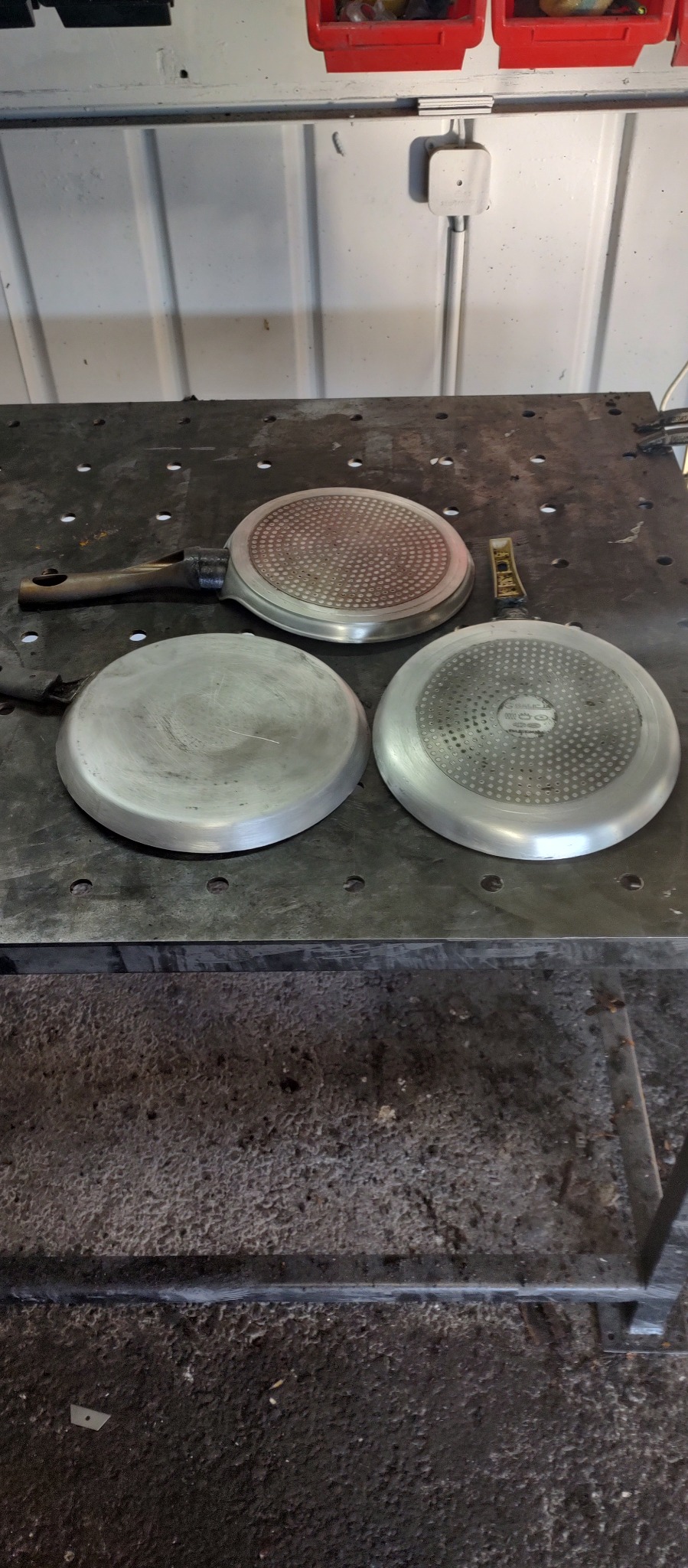 Trzy aluminiowe formy do gofrów o różnych wzorach powierzchni, leżące na metalowym stole warsztatowym z widocznymi śladami użytkowania.