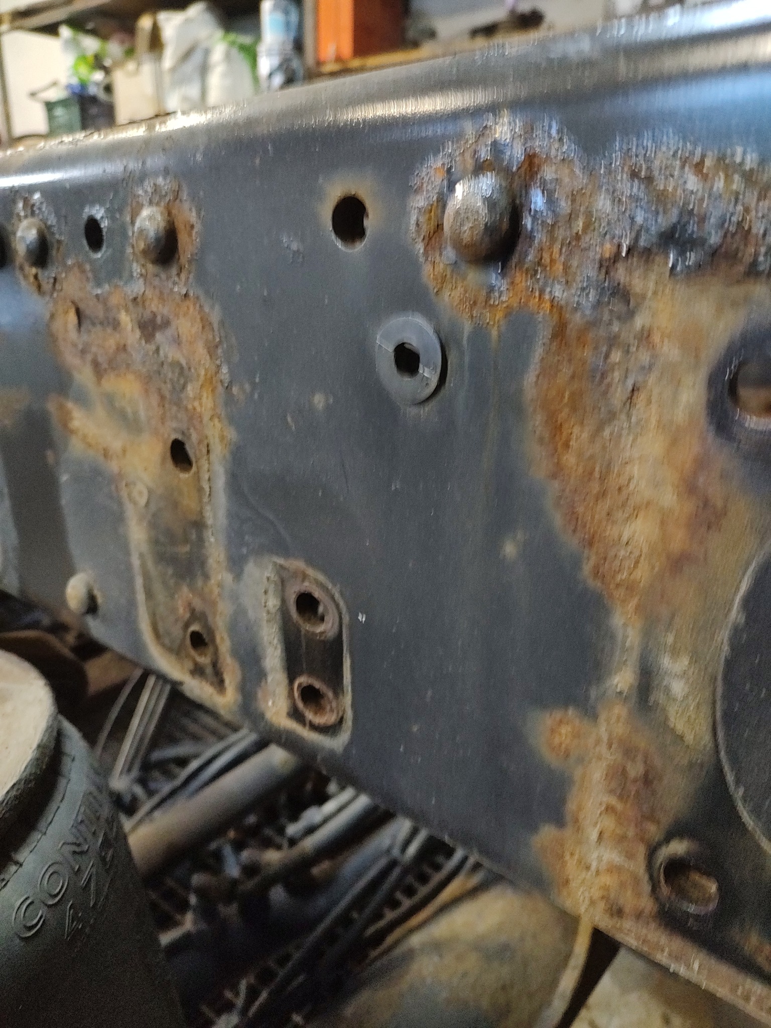 Fragment ramy pojazdu z widocznymi śladami korozji i starym lakierem, z bliska.