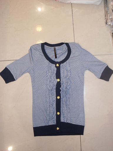 Damska bluzka w paski z krótkim rękawem, ozdobiona falbankami i złotymi guzikami, leżąca na marmurowej podłodze.