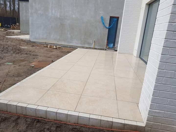 Wyłożony jasnymi płytami taras przy nowoczesnym domu z białej cegły, widoczne przygotowania do dalszych prac wykończeniowych.