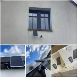 Zewnętrzna kamera monitoringu z panelem solarnym marki EZVIZ, zamontowana na elewacji budynku pod oknem. Widoczne pudełka z zestawami kamer.