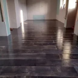 Ułożona, ciemna, błyszcząca podłoga z płytek imitujących drewno w trakcie remontu; ściany częściowo wykończone płytami kartonowo-gipsowymi, widoczne szczeliny i niedokończone łączenia.