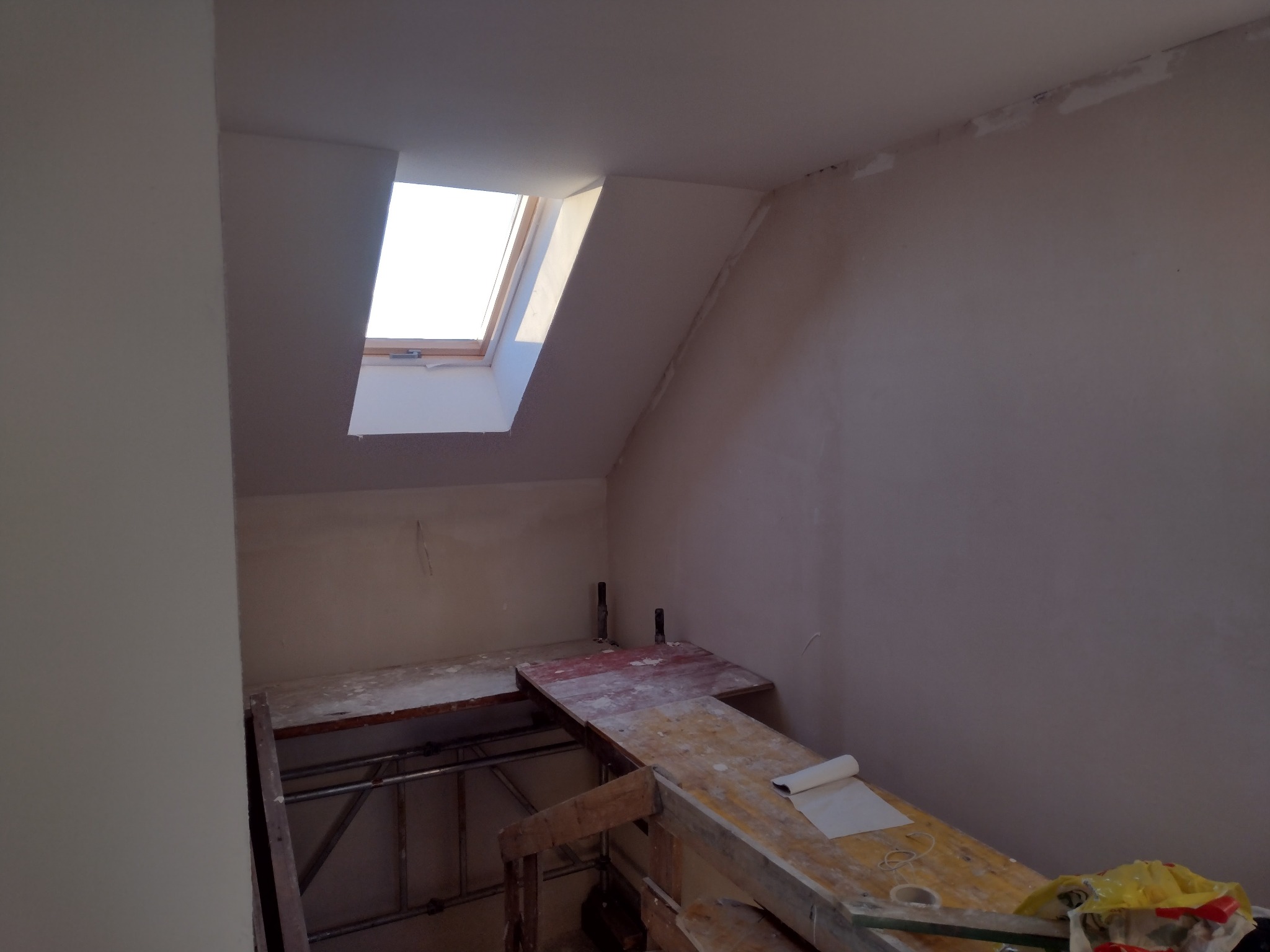 Poddasze w trakcie wykańczania: widoczne rusztowanie, okno dachowe, ściany przygotowane do malowania, częściowo wyszpachlowane, z widocznymi śladami po szpachli.