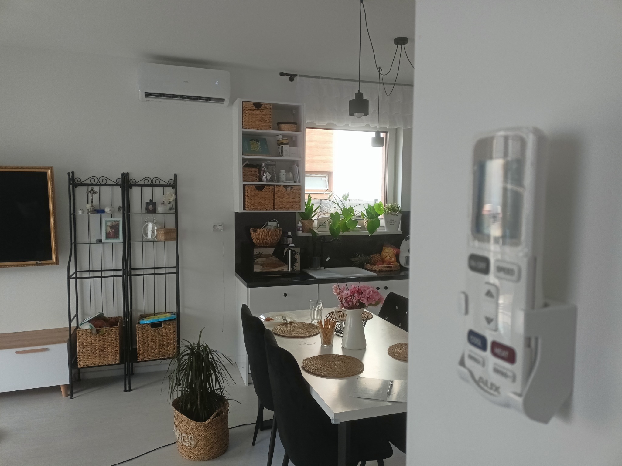 Nowoczesny salon z zamontowanym klimatyzatorem na ścianie, widoczny pilot do klimatyzacji na ścianie, stół jadalny i elementy dekoracyjne.