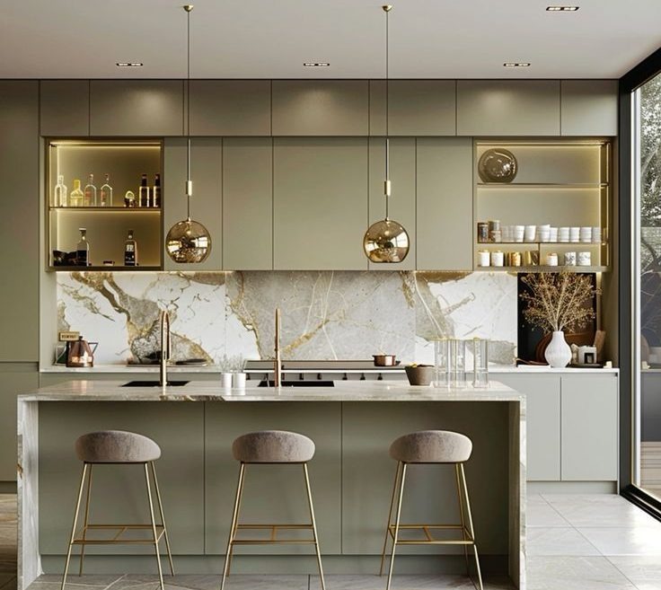 Elegancka kuchnia w odcieniach zieleni z marmurowym blatem i złotymi akcentami oświetlenia, podkreślona przez trzy nowoczesne hokery.