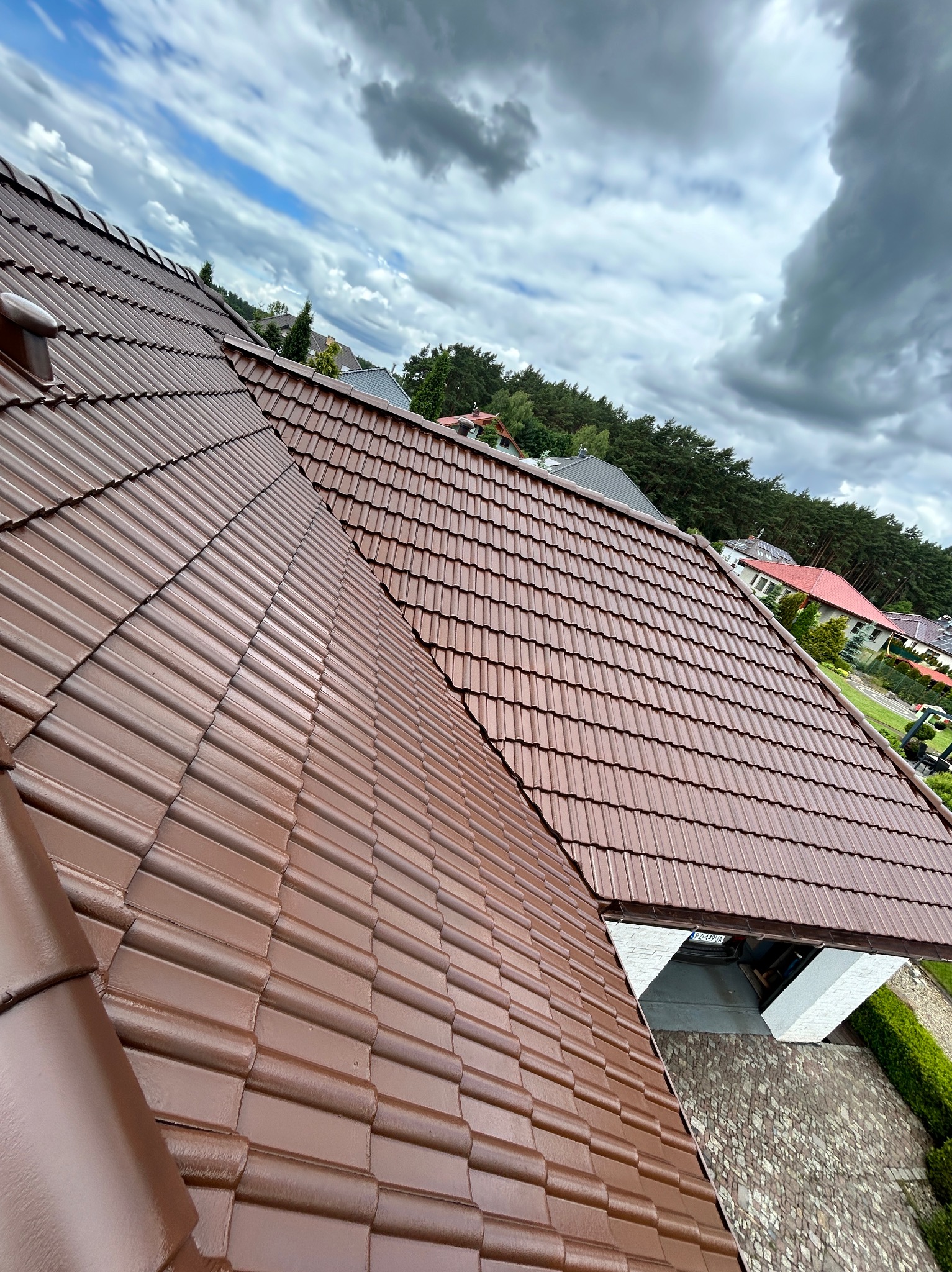 Ciemnobrązowy dach z dachówki ceramicznej, świeżo po renowacji, widok z góry na tle pochmurnego nieba. Widoczne detale tekstury dachówki i otoczenie domu.