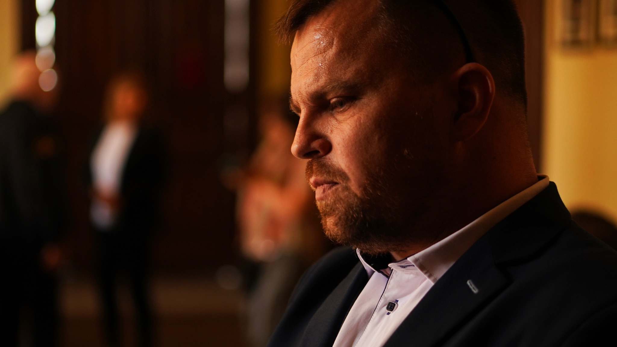 Portret biznesowy mężczyzny w garniturze, profil, zamyślony wyraz twarzy, osoby w tle