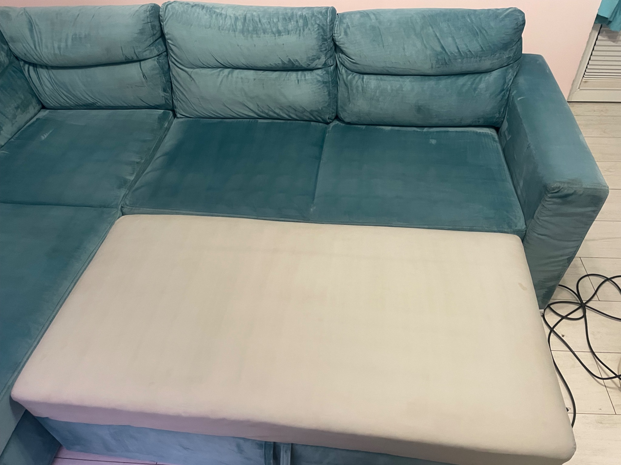 Turkusowa sofa narożna z wysuniętym, jasnym siedziskiem, na którym widoczne są delikatne plamy.