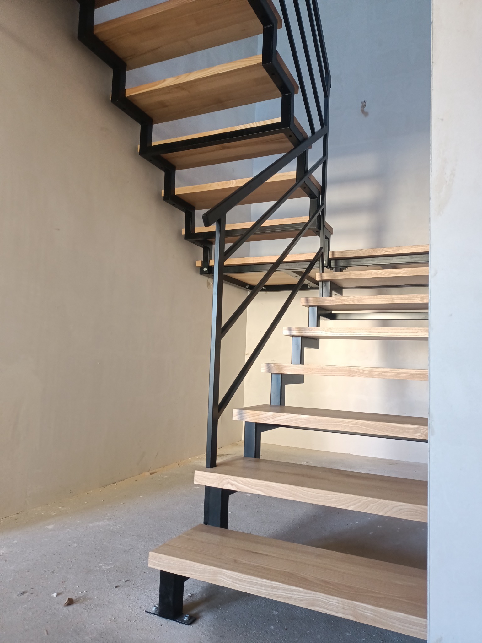 Nowoczesne schody drewniane z czarną metalową konstrukcją w surowym wnętrzu, widok z dołu.