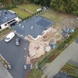 ECOFAB - Widok z lotu ptaka na dwa domy jednorodzinne z panelami słonecznymi na dachach, biały bus serwisowy zaparkowany na podjeździe, teren wokół w trakcie prac wykończeniowych.