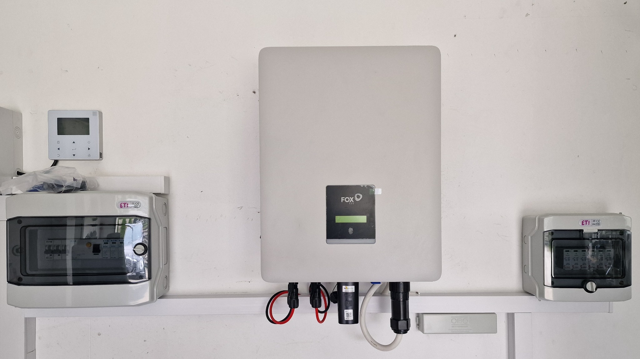 Zamontowany inwerter Fox ESS na białej ścianie, obok skrzynki bezpiecznikowe ETI i panel sterowania, instalacja fotowoltaiczna.