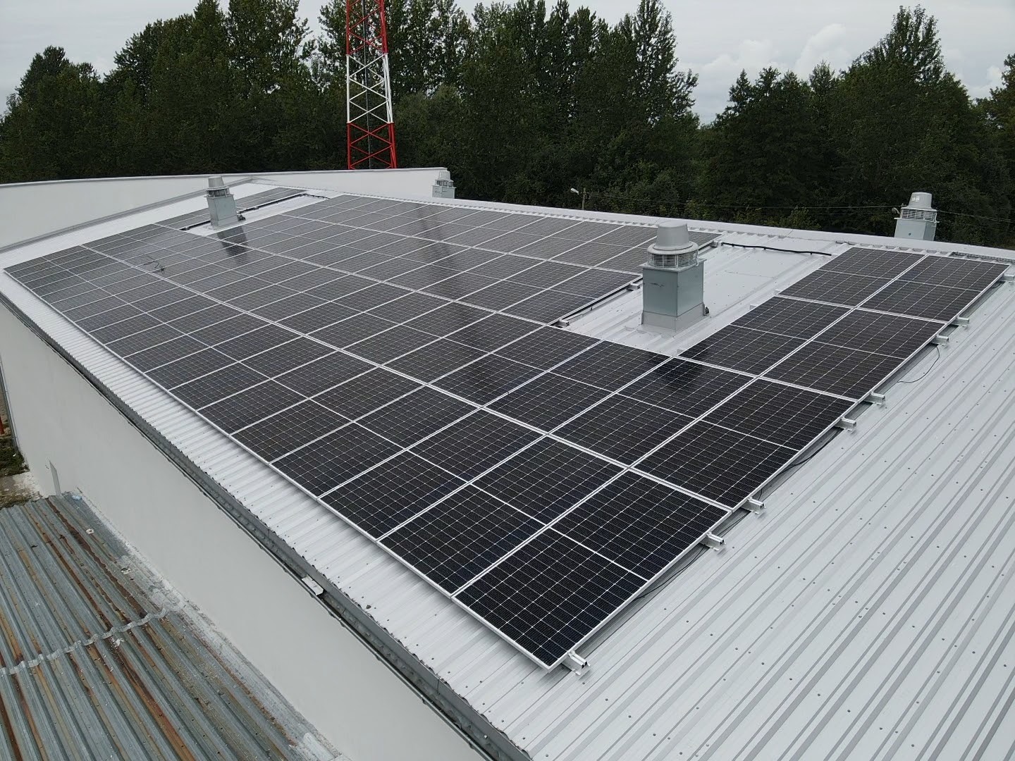 Instalacja paneli słonecznych na dachu przemysłowym w Słupsku, widoczne kominki wentylacyjne i maszt telekomunikacyjny w tle.