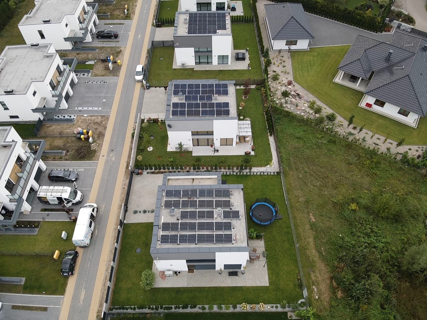 Widok z góry na osiedle domów jednorodzinnych z panelami słonecznymi na dachach, trawnikami i zaparkowanymi samochodami.
