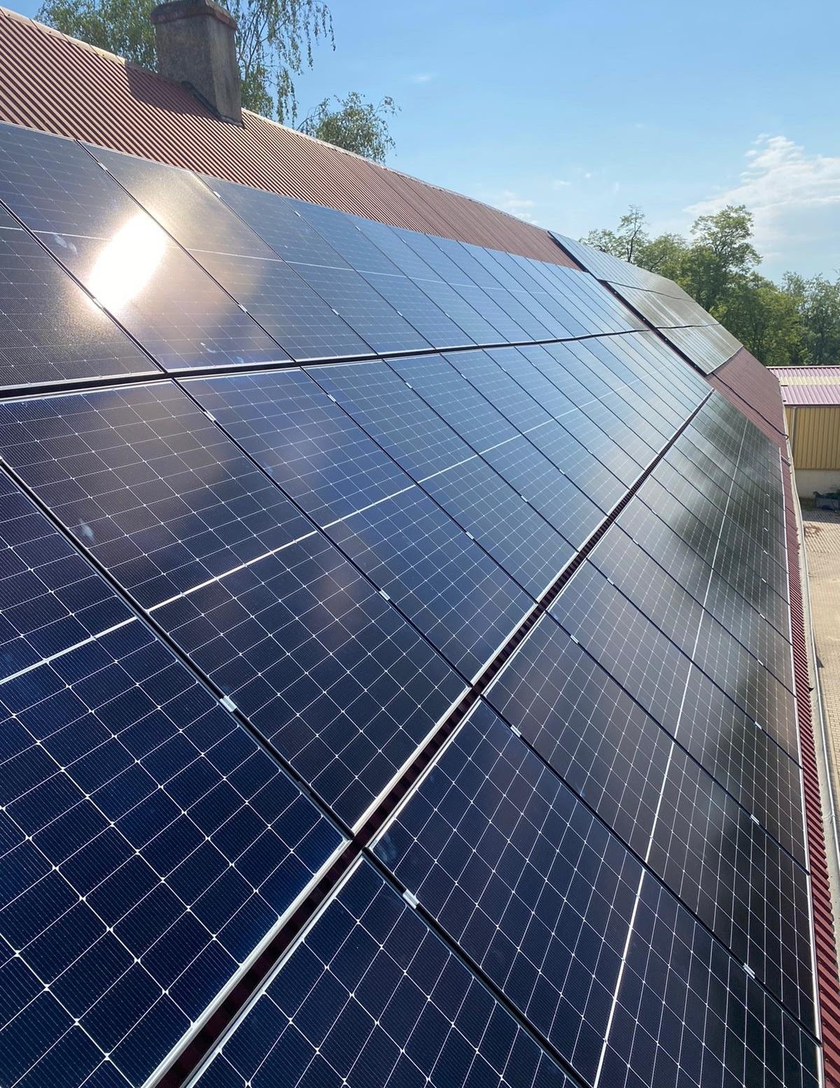 Panele słoneczne na dachu z czerwonej dachówki, odbijające słońce, widok z dołu pod kątem.