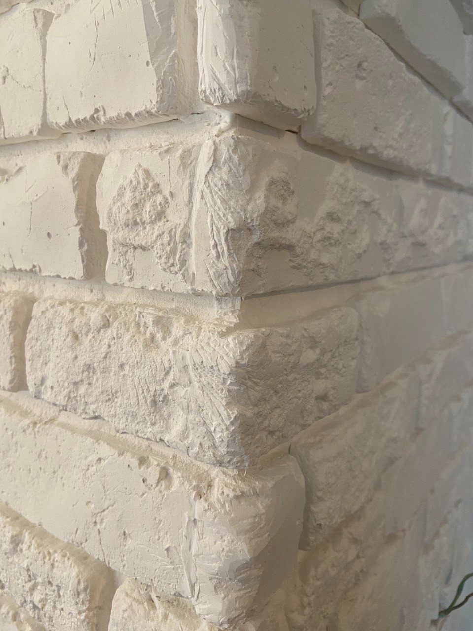 Biała ściana z cegieł dekoracyjnych, imitujących stary mur, z wyraźną fakturą i widocznym narożnikiem. Tekstura podkreślona światłem.