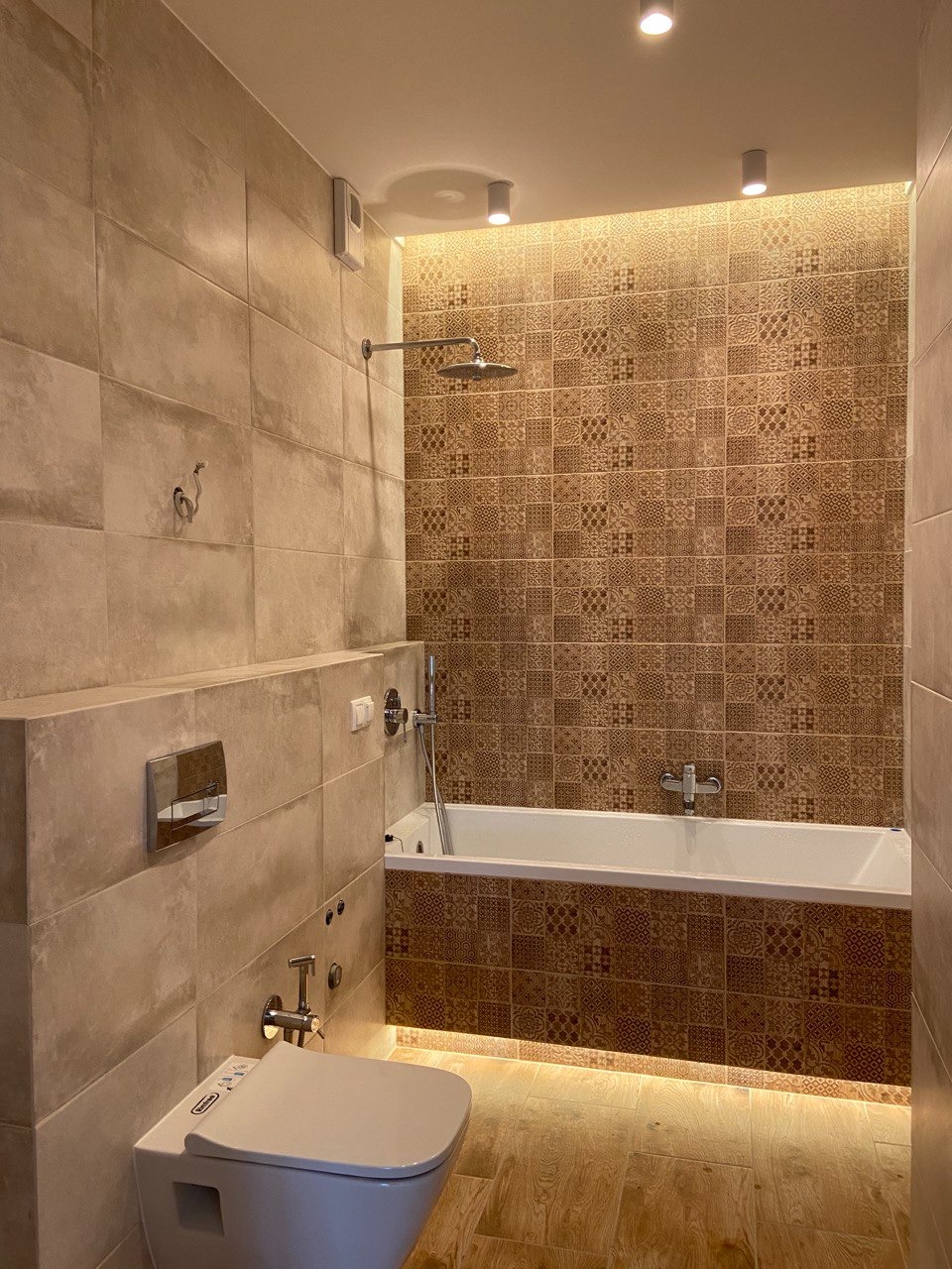 Elegancka łazienka z beżowymi płytkami, mozaiką nad wanną i podświetleniem LED. Nowoczesna toaleta podwieszana i deszczownica tworzą spójny wystrój.