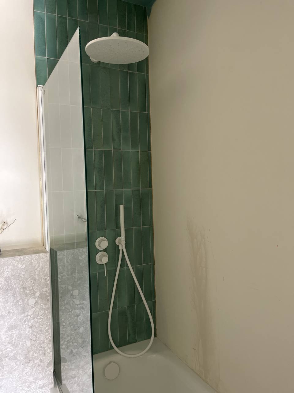 Nowoczesna łazienka z zielonymi płytkami, białą armaturą i szklanym panelem prysznicowym. Minimalistyczny design, pionowe płytki, jasne wnętrze.