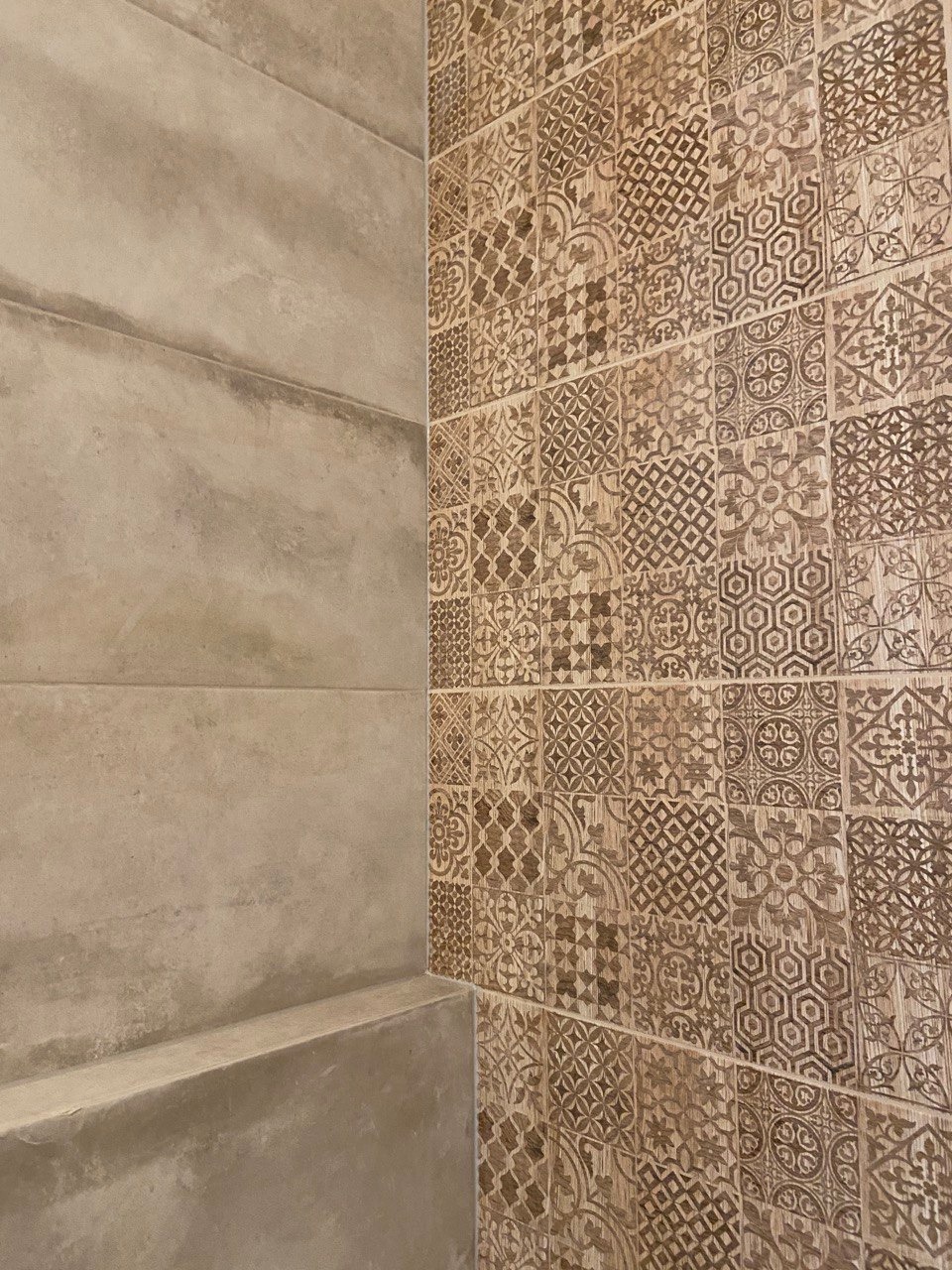 Detal prezentujący połączenie dwóch rodzajów okładzin ściennych: gładkich, beżowych płyt imitujących beton oraz dekoracyjnych płytek w odcieniach brązu z geometrycznymi i roślinnymi wzorami...