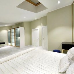 Roman Berehovyi - Jasna sypialnia z kremowymi ścianami, białymi drzwiami i podłogą, niebieskim zagłówkiem łóżka i oknem dachowym w suficie.
