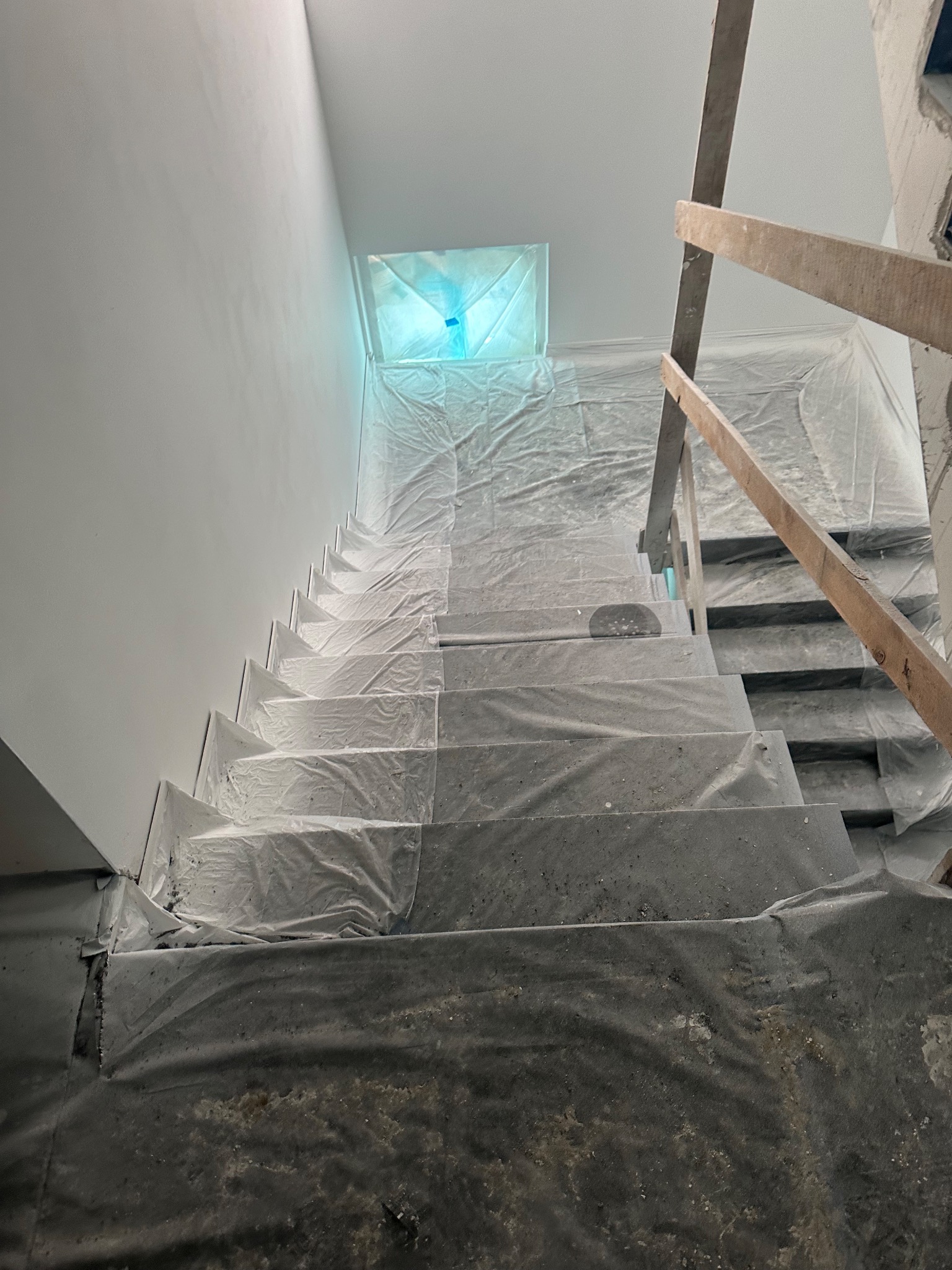 Schody zabezpieczone folią malarską podczas prac remontowych, świeżo pomalowana ściana w tle, widoczne rusztowanie.