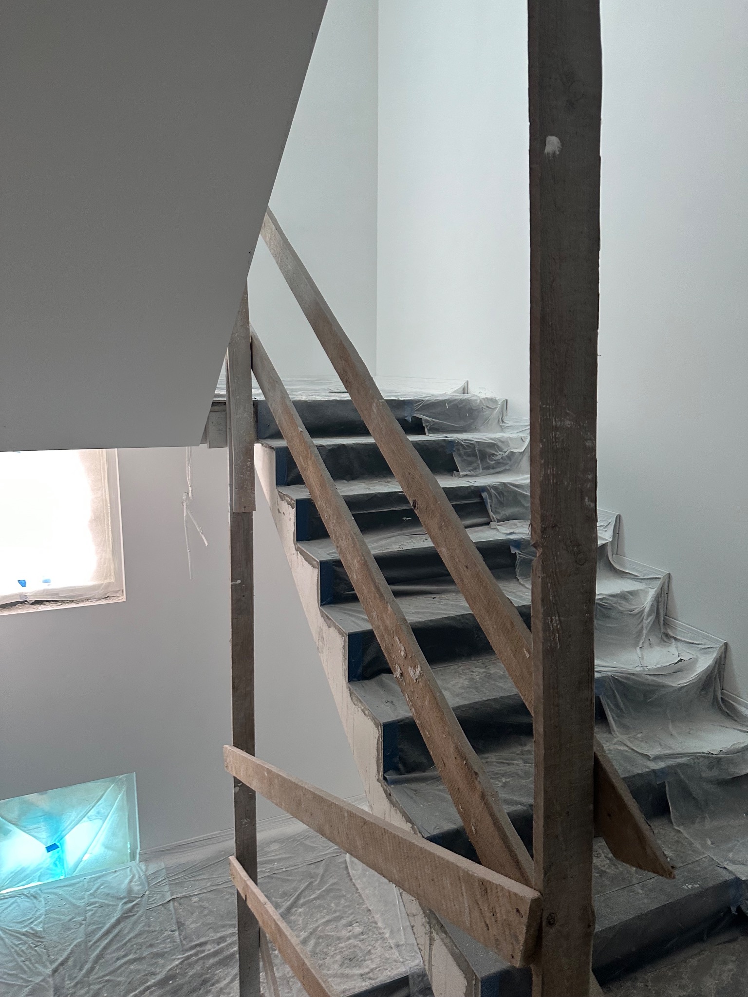 Schody zabezpieczone folią malarską podczas prac wykończeniowych, widoczna drewniana konstrukcja ochronna i świeżo pomalowane ściany na biało.