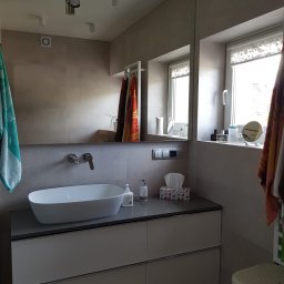 GOLD MAJSTER sp. z o.o. - Nowoczesna łazienka z owalną umywalką nablatową, szarą szafką pod umywalką, dużym lustrem, oświetleniem punktowym i akcesoriami łazienkowymi na parapecie okna.