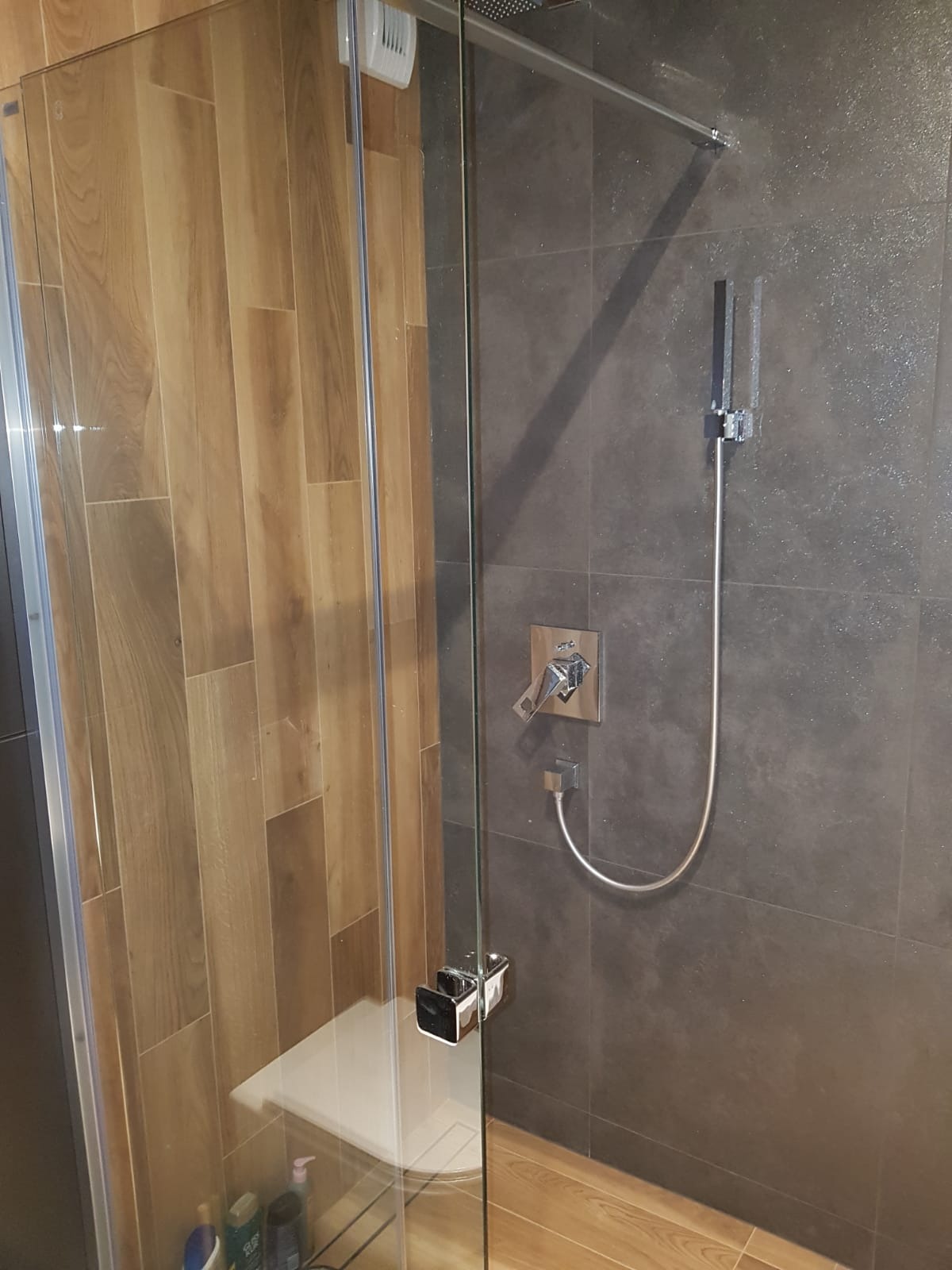 Kabina prysznicowa z drewnopodobnymi i grafitowymi płytkami w łazience w Gliwicach, widoczna bateria i półka pod prysznicem.