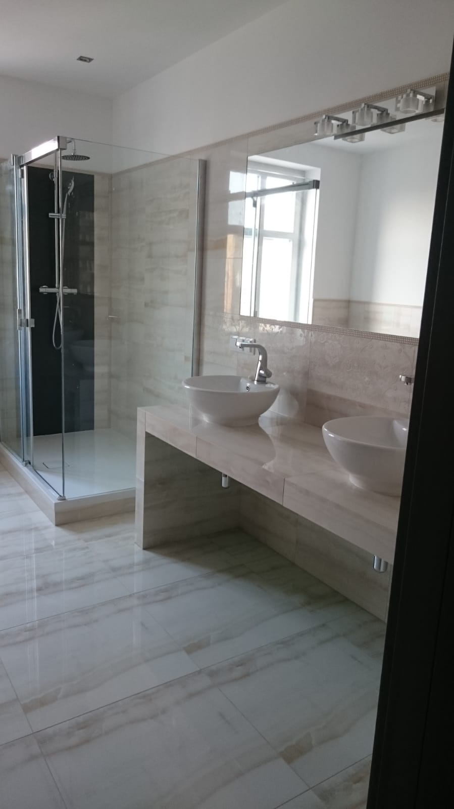 Nowoczesna łazienka z kabiną prysznicową typu walk-in i podwójną umywalką nablatową na blacie z płytek imitujących marmur.