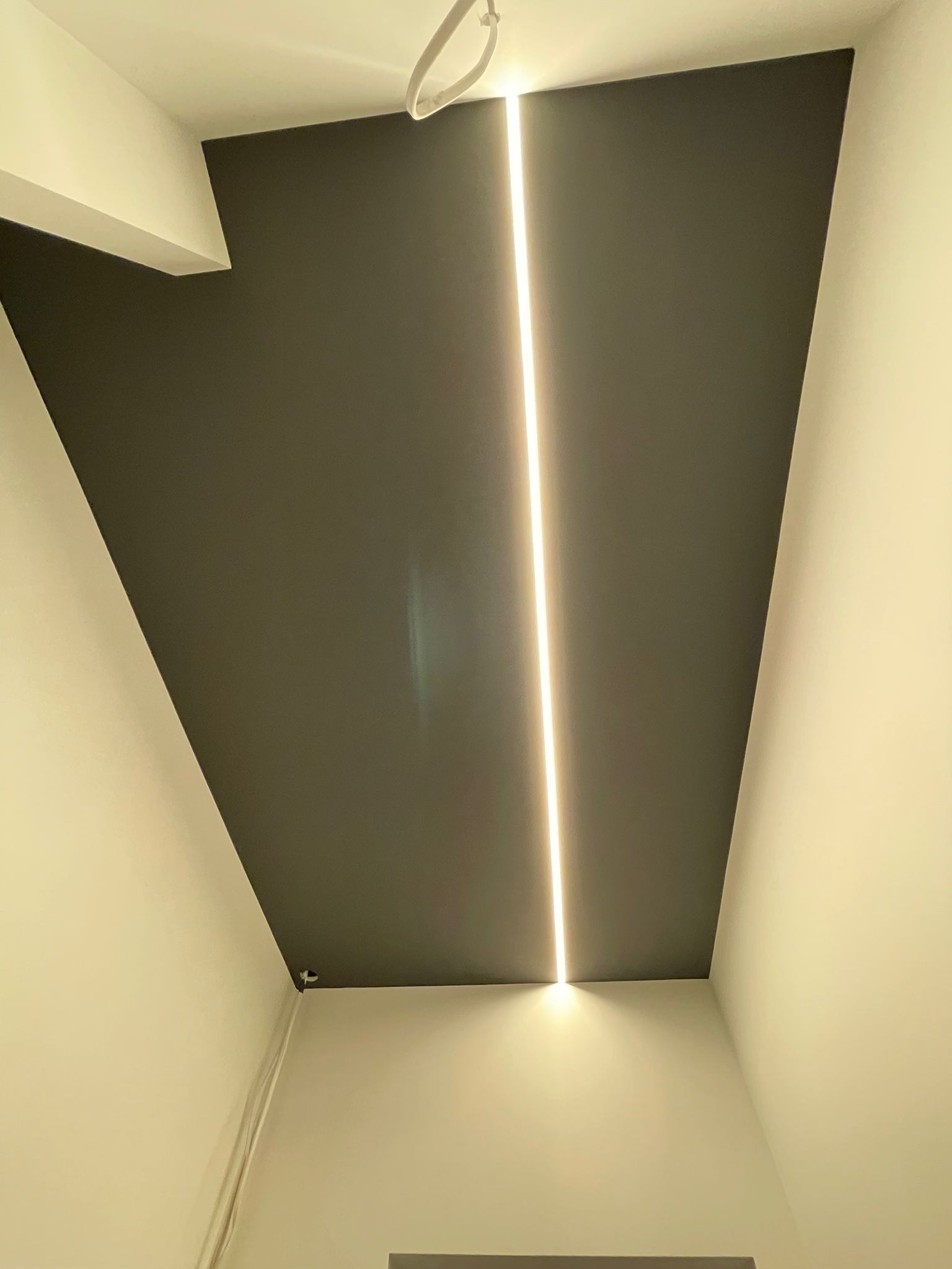 Nowoczesne wnętrze z ciemnoszarym sufitem i pionową linią świetlną LED, kontrastujące z jasnymi ścianami.